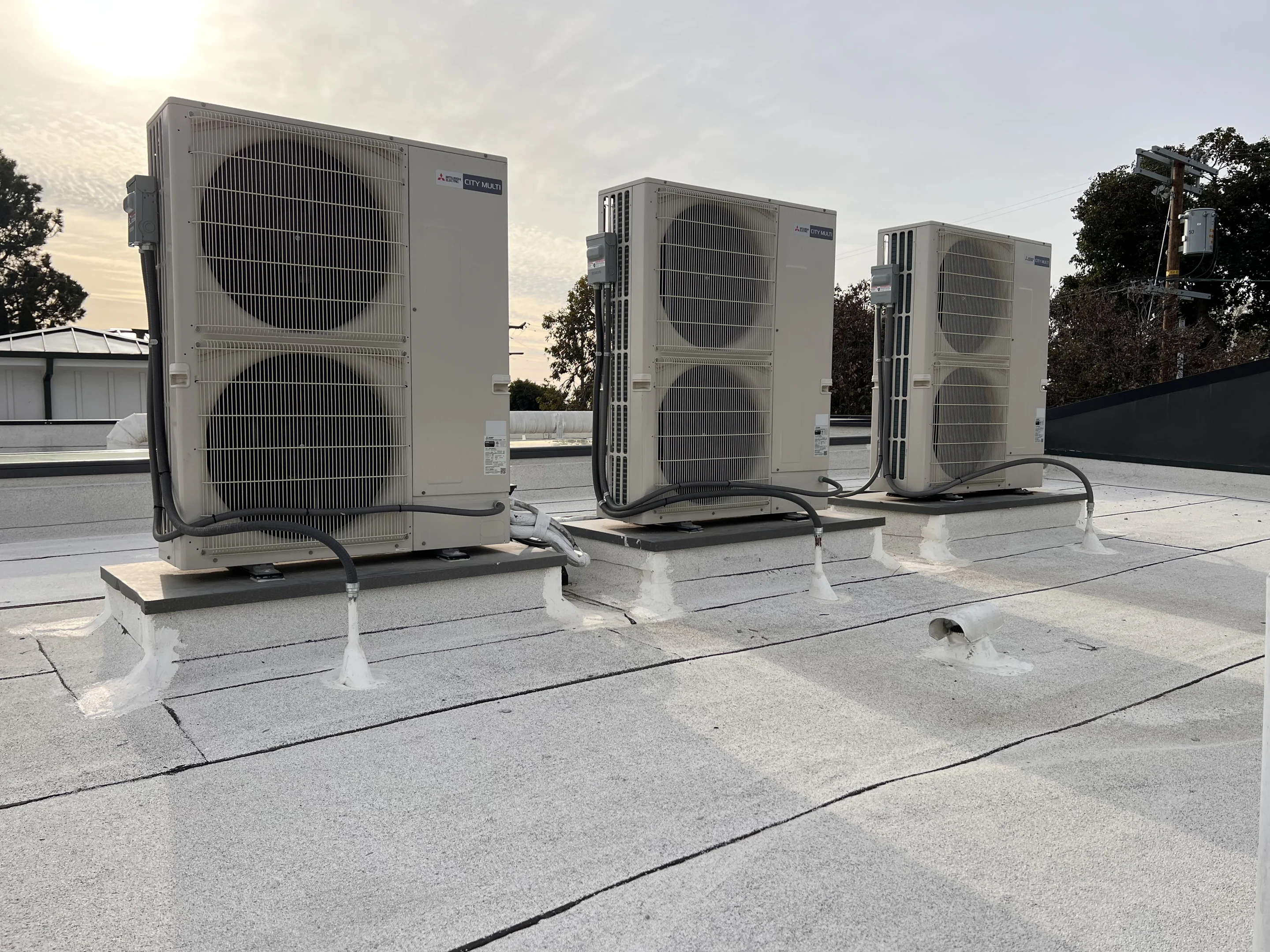 Three outdoor units on a rooftop at sunset.